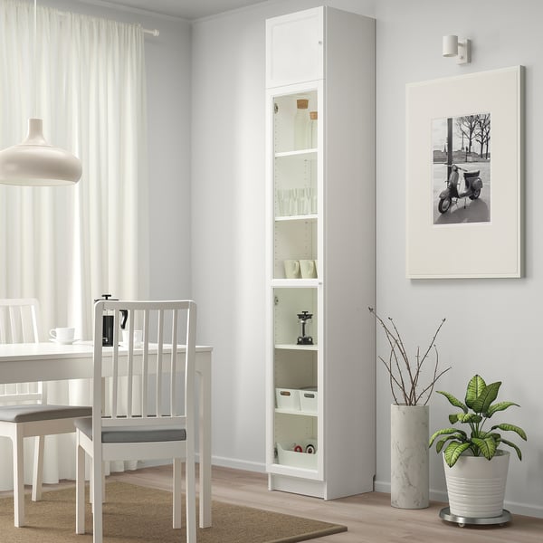 Minimalistyczna jadalnia z wysoką białą szafką eksponującą szkło, obok białego krzesła i oprawionego zdjęcia.