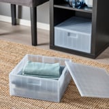 Dwa plastikowe pudełka z niebieskimi ręcznikami, jedno otwarte, ułożone pod szarymi półkami.