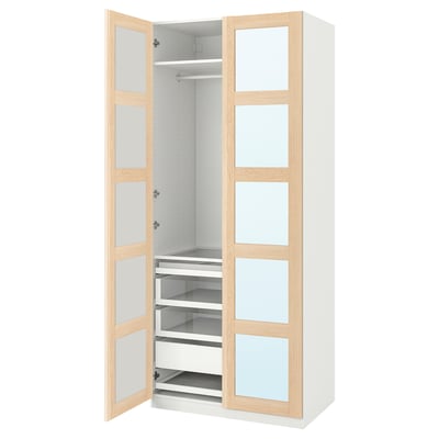 Otwarta biała szafa PAX z akcentami z jasnego drewna. Szklane drzwi, szuflady, półki i miejsce do zawieszania.