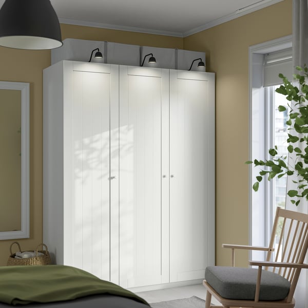 Dobrze zorganizowany kącik sypialniany z dużą szafą ikea PAX, eleganckimi uchwytami, lustrem i drewnianym fotelem bujanym.