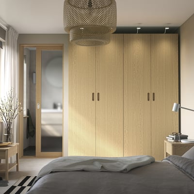Nowoczesna wysoka szafa PAX z jasnego drewna, elegancki design, szara pościel, wisząca oprawa oświetleniowa i stolik boczny z dekoracją.