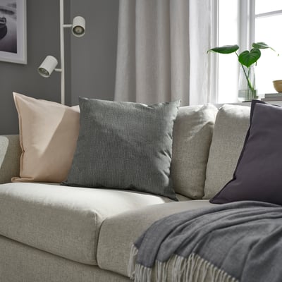 Salon z jasnoszarą sofą, antracytowymi poduszkami i zielonymi roślinami. Albo szara sofa, poduszki i rośliny w nowoczesnym, minimalistycznym salonie.
