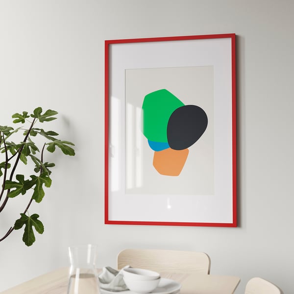 Nowoczesny czerwony wydruk artystyczny na szarej ścianie nad stołem jadalnym z białymi naczyniami. Zielona roślina po lewej.