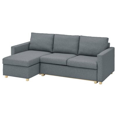 Szara sofa roczna IKEA SALTSJÖBADEN z drewnianymi nogami. Ma kształt litery L, wygodne poduszki i jest wykonany z recyklingowanego poliestru.