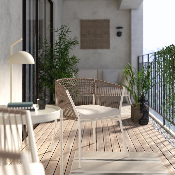 Nowoczesny balkon z jasnobeżowym wiklinowym krzesłem SEGERÖN, małym stolikiem i roślinami doniczkowymi. Betonowe tło ściany.