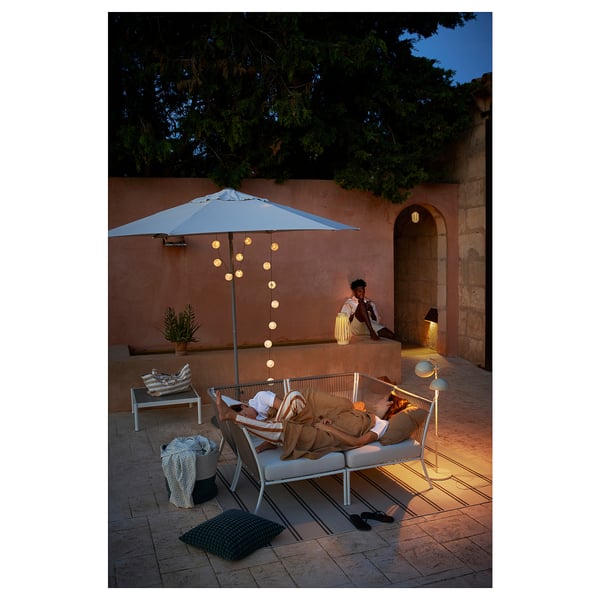 Patio na świeżym powietrzu z meblami SEGERÖN, sofą, stołem, lampą i parasolami.