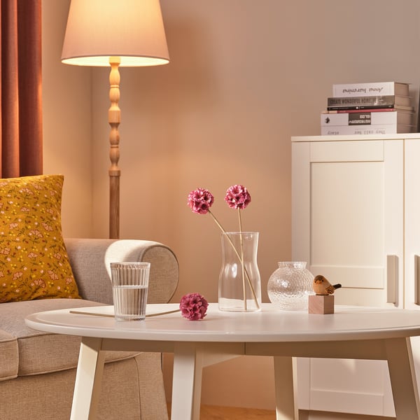 Przytulny salon z beżowymi ścianami, wazonem na stole z kwiatami i abażurem.