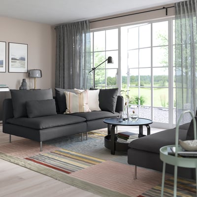Nowoczesny salon z szarą sofą segmentową SÖDERHAMN, dywanem w paski, dużym oknem i eleganckim wystrojem.
