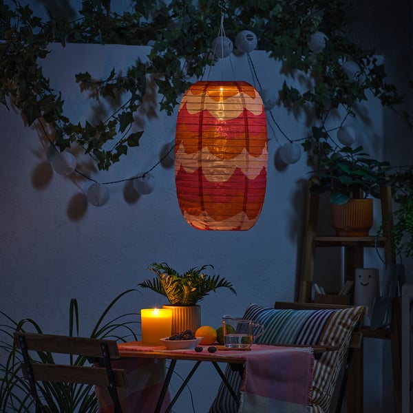 Nocne patio z latarnią, świecami, roślinami, krzesłami i łańcuchami świetlnymi.