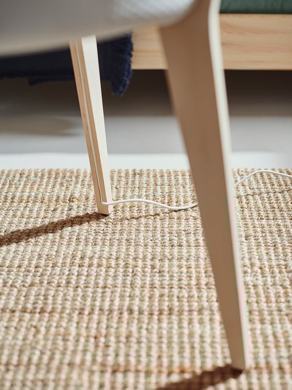 Beżowy tkany dywan pod drewnianymi meblami. Cienki biały sznurek krzyżuje dywan. Nowoczesny, minimalistyczny design.