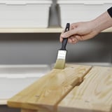 Ręcznie szczotkuje drewnianą deskę olejem ochronnym, nadając jej połysk i trwałość.