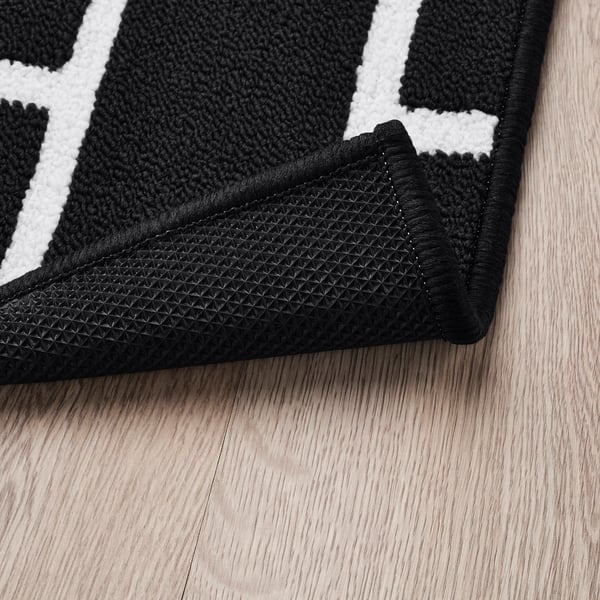 Dywan w czarno-białą kratkę na drewnianej podłodze. Widoczny antypoślizgowy spód.