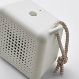 Kompaktowy, przenośny głośnik z plecioną rękojeścią, gładkim wykończeniem i licznymi otworami na wyjście audio.