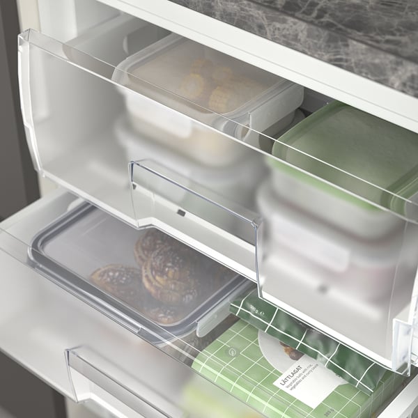 Mała lodówka z 3 szufladami, do przechowywania różnych produktów spożywczych. W szufladach znajdują się wypieki i zielone pojemniki.