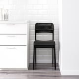 Black plastic chair with perforated design, suitable for stacking and indoor use, positioned near white cabinets.
