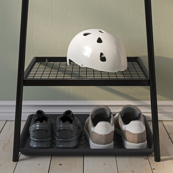 Black metal shoe rack stores two pairs of sneakers and a white helmet on top shelf, perfect for hallways.