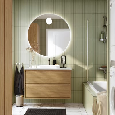 Modern bathroom with oak ÄNGSJÖN vanity, green tiles, glass shower, and beige towel.