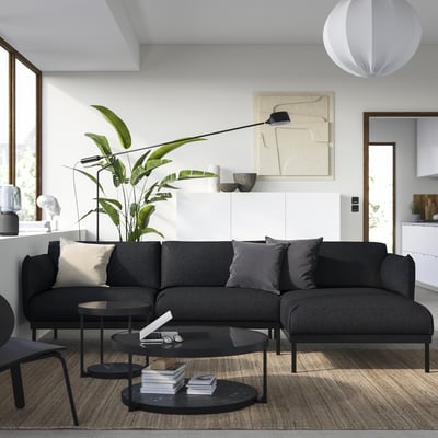 Modern living room with gray ÄPPLARYD sofa, pillows, black tables, plant, art, pendant lamp, wooden floor.