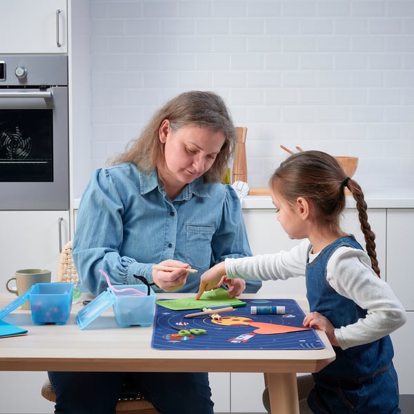 Woman and child crafting on table protected by AFTONSPARV pad, made from recycled polyester.