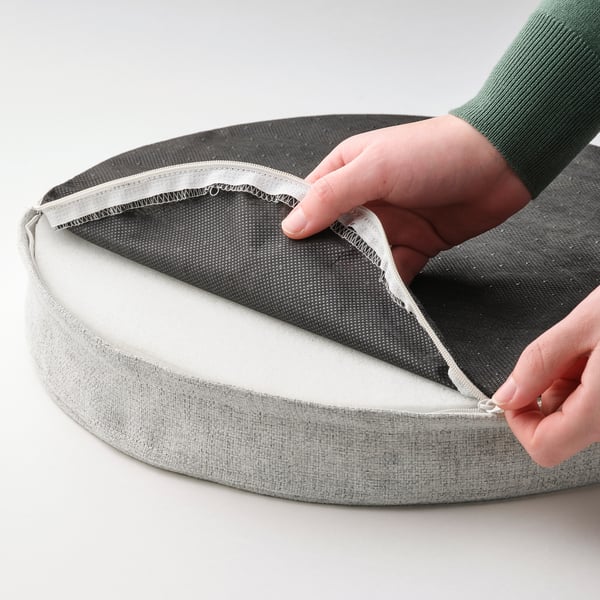 Hand opening gray circular cushion, revealing memory foam and non-slip backing.