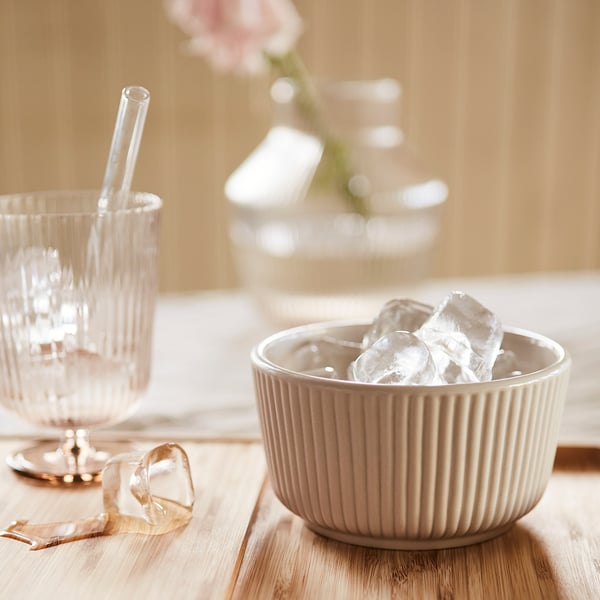 Light brown glass goblet and bowl with ice on wooden table.