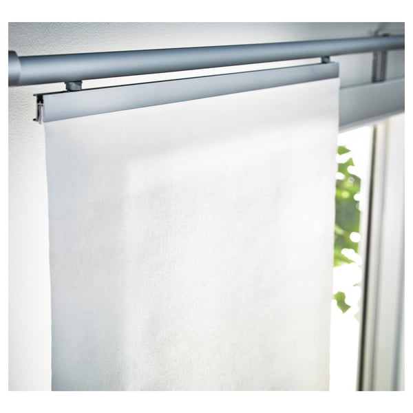 White roller blind partially rolled up, mounted on a minimalist silver track above a window. Lightly filters outside light.