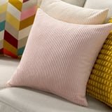 Round, pink corduroy cushion with vertical lines, larger than yellow patterned pillow on stripe background.