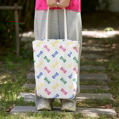 Person holding large ikea tote bag outdoors near garden path.