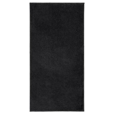 A black rectangular BACKMÅRA bath mat made of recycled polyester, featuring a soft pile and latex backing.