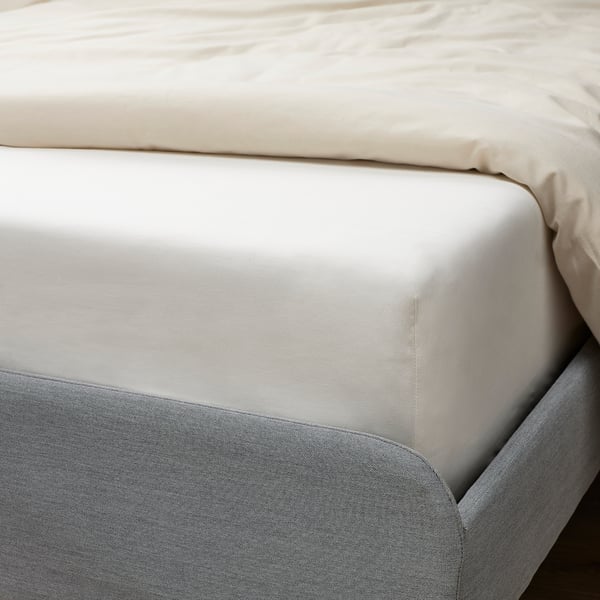A crisp white fitted sheet on a bed, made of organic cotton, securely fitted with elastic edging around a thick mattress.