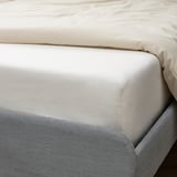 A crisp white fitted sheet on a bed, made of organic cotton, securely fitted with elastic edging around a thick mattress.