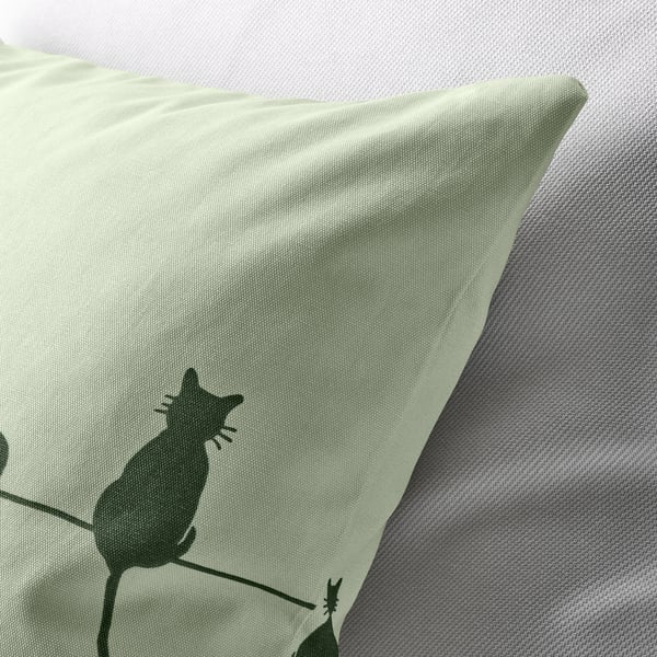 Soft, green, cat-themed pillowcase on cozy white bedding. Zipper detail visible.