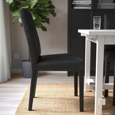 Black leather dining chair with wooden legs under a table on a woven rug.