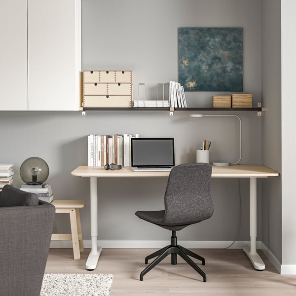 Home office with wooden desk, laptop, ergonomic chair, wall art, and bookshelf.