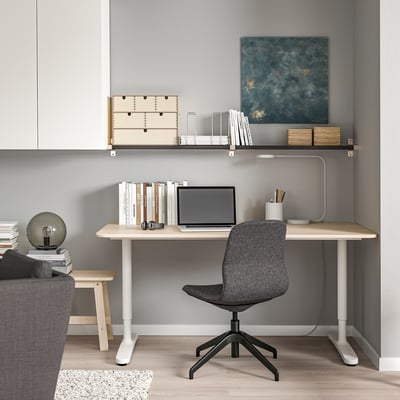 Home office with wooden desk, laptop, ergonomic chair, wall art, and bookshelf.