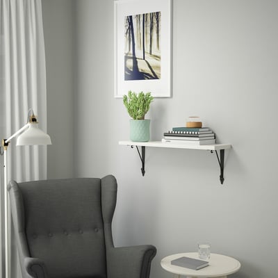 Minimalist decor: BERGSHULT wall shelf holds books, plant near grey chair. Small, white, rectangular, supported by black metal brackets.