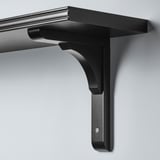 Black metal wall shelf with angled bracket attached to wall. Sleek design with smooth and beveled edges.