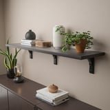 Wall shelf with black brackets holds decorative items like plants, books, and vases.
