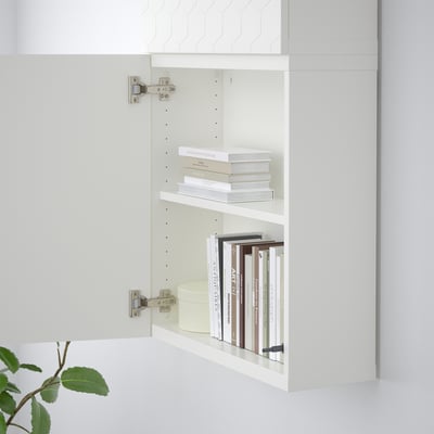 White wall-mounted cabinet with two shelves filled with books, featuring adjustable feet and metal hinges.