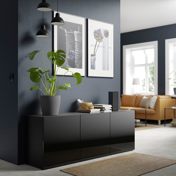 Modern living room with dark gray BESTÅ sideboard, large green plant, black pendants, framed art, orange sofa, and rug.