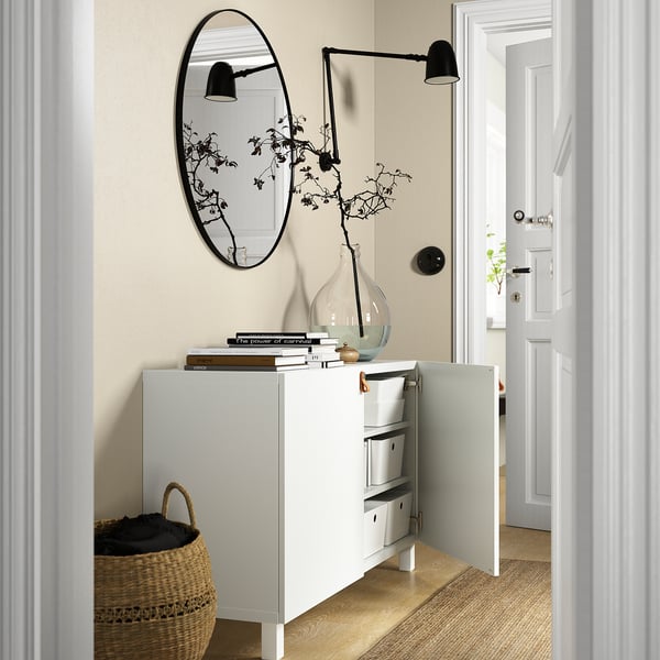 A modern white sideboard with adjustable shelves and soft-close doors, styled with books, a vase, and a mirror above.