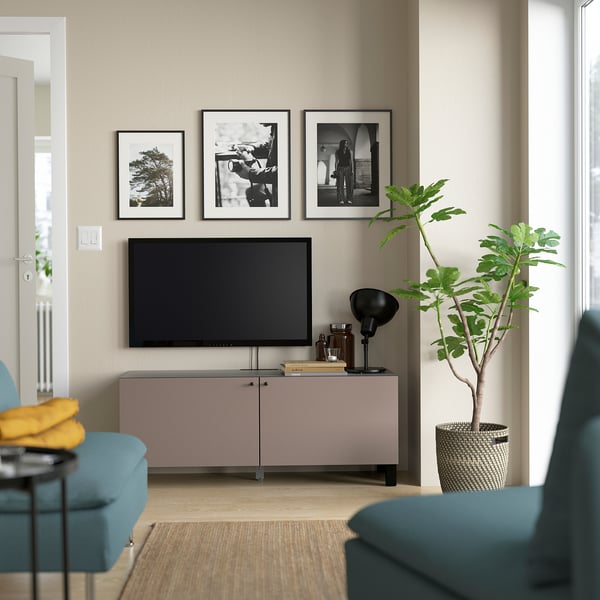 Grey BESTÅ tv stand with adjustable shelves and color cushions. Flanked by teal chairs and a large green plant.