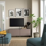 Grey BESTÅ tv stand with adjustable shelves and color cushions. Flanked by teal chairs and a large green plant.