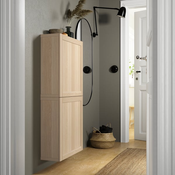 Wooden BESTÅ cabinet with adjustable hinges, soft-closing door, floor-to-ceiling height, decorative items above, basket below.