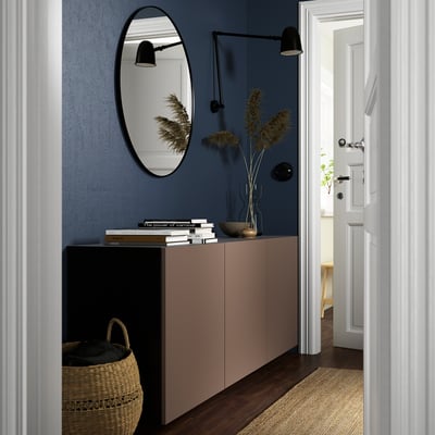 Modern living room with BESTÅ cabinet, books, plants, mirror, and lamps against blue wall.