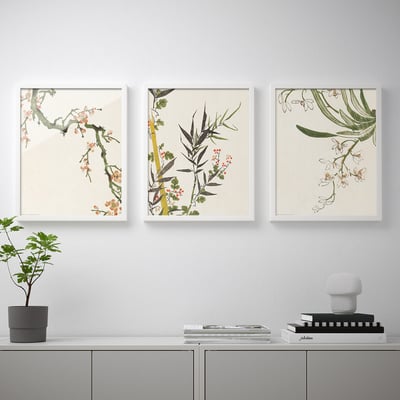 Three floral prints hang above a sideboard with a plant and books.