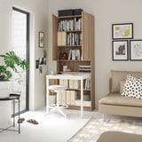 Home office setup featuring BILLY bookcase with desk, white and wood, storing books and supplies, paired with a beige sofa and plant.