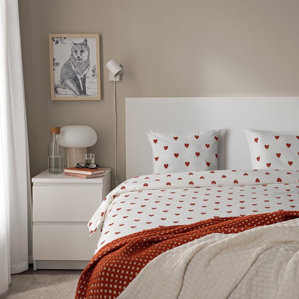 Cosy bedroom with BJÖRNBÄRBUSKE duvet featuring red hearts, white headboard, bedside table with lamp, books, glass, and fox picture.