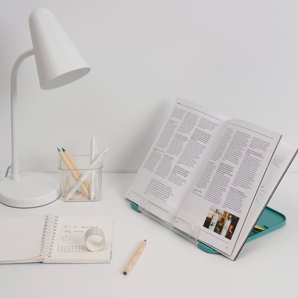 Study setup with lamp, open book, notepad, and pencils. Book holder angles pages neatly.