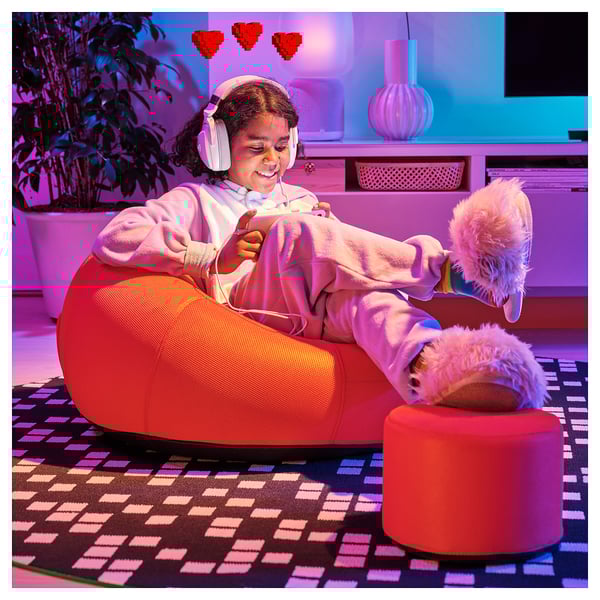 Girl in red chair, headphones, smiling.